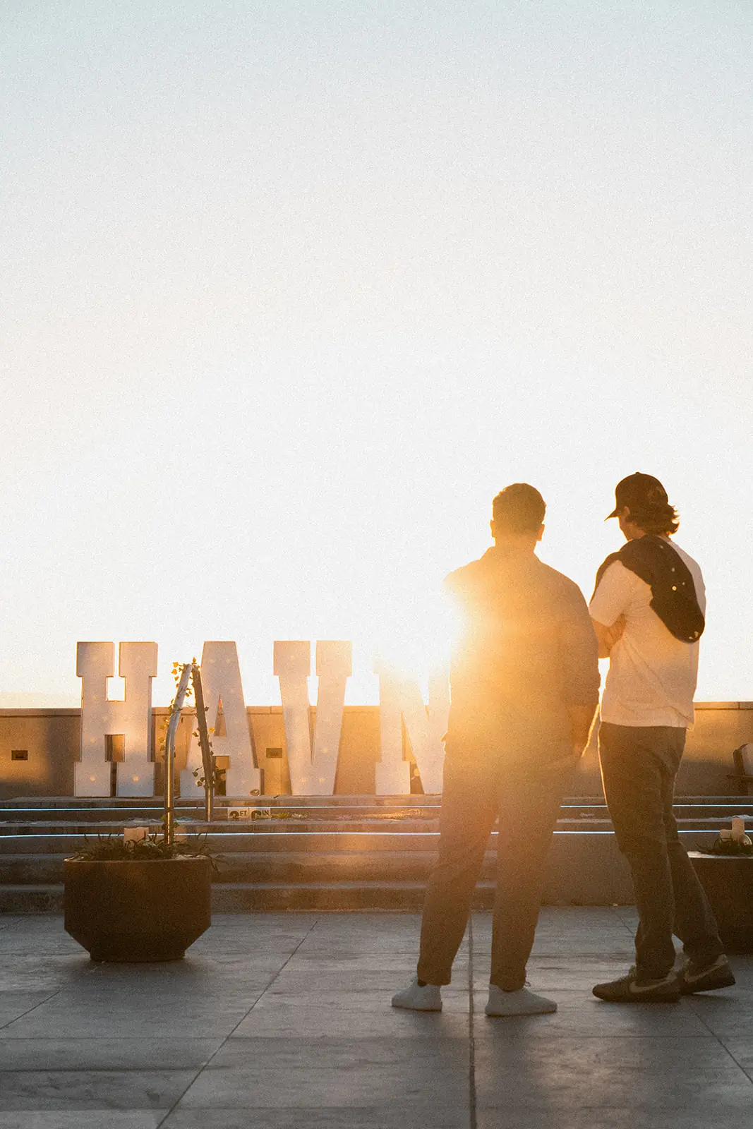 Two members on the HAVN rooftop at sunset beside the illuminated HAVN marquee